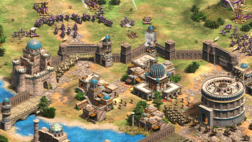 Fight epic battles and lead your people to victory in Age of Empires 2, one of the best RTS games. In this screenshot, in the lower half of the image, you can see a huge massive base built of stones in a top-down view, with various oriental buildings. In the lower right of the frame, several units patrol in formation on the way to the battle, which is shown in the upper half of the frame. There we see both in the upper left corner and in the upper right corner many enemy purple-colored cavalry and infantry. Behind them are three trebuchets set up to bombard the base wall with stone. At the bottom of the picture, there is a light blue river with a stone bridge across it in the lower left corner.