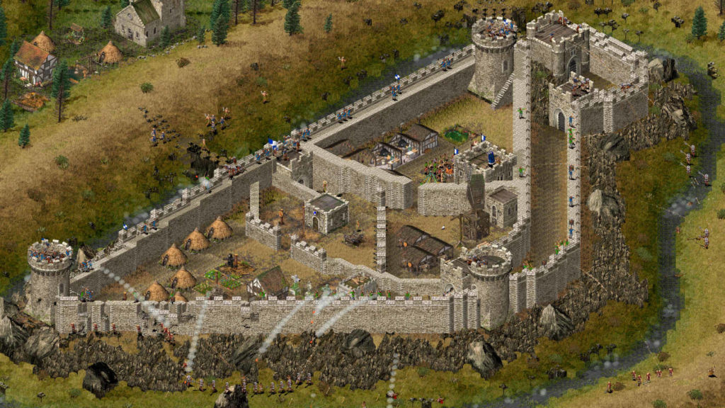 Here is a screenshot from the game Stronghold, where you can see a huge castle in a top-down view and in 2D graphics, which is currently being attacked by enemies all around by daylight. The castle has a large tall stonewall all around and includes three large, round castle towers on which archers are positioned, shooting arrows at the attackers. Around the triangle-shaped castle is a moat. In the upper left corner of the frame, two more medieval buildings can be seen, as well as a field with a straw bale. Next to it are several fir and deciduous trees. 