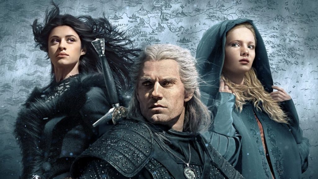 Here we see the main characters, who once again appear as the cast of The Witcher. They are staggered in a triangular formation in this image, looking in different directions. At the very front, the Witcher Henry Cavill is pictured in a close-up. He wears black knight's armor and has a longsword on his back. His gaze goes out of the picture to the left. Behind him on the left and a little higher is Anya Chalotra with long black hair blowing in the wind and a black fur coat. She looks out of the picture to the right. Right at the same height stands Freya Allan in a turquoise coat. She has blond curly hair, which is partially covered by a large hood that she wears over her head. She is looking in the same direction as the protagonist. In the background we see the identical black and white silver shimmering landscape map with various symbols like in the Close-Up Image from Henry Cavill.