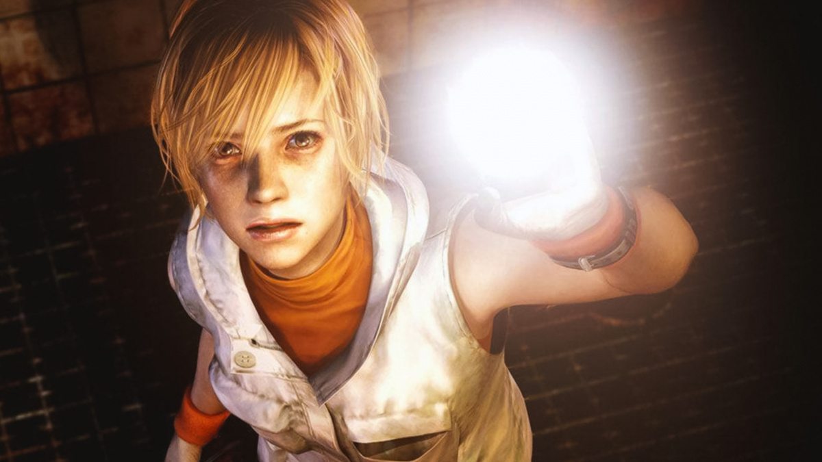 In the Silent Hill Game Sequel, Cheryl might be walking around with a flashlight again, as illustrated in this close-up. We look from above at the protagonist with her short blonde hair, orange collared sweater, and white vest. She stands on a black metal scaffolding in the darkness and looks with an anxious gaze in our direction. As she does so, she holds up a flashlight with her hand, shining it in our direction. Behind her is a wall of red brick, which can be seen in the crop at the top of the image. Her face is illuminated by the light of the flashlight.