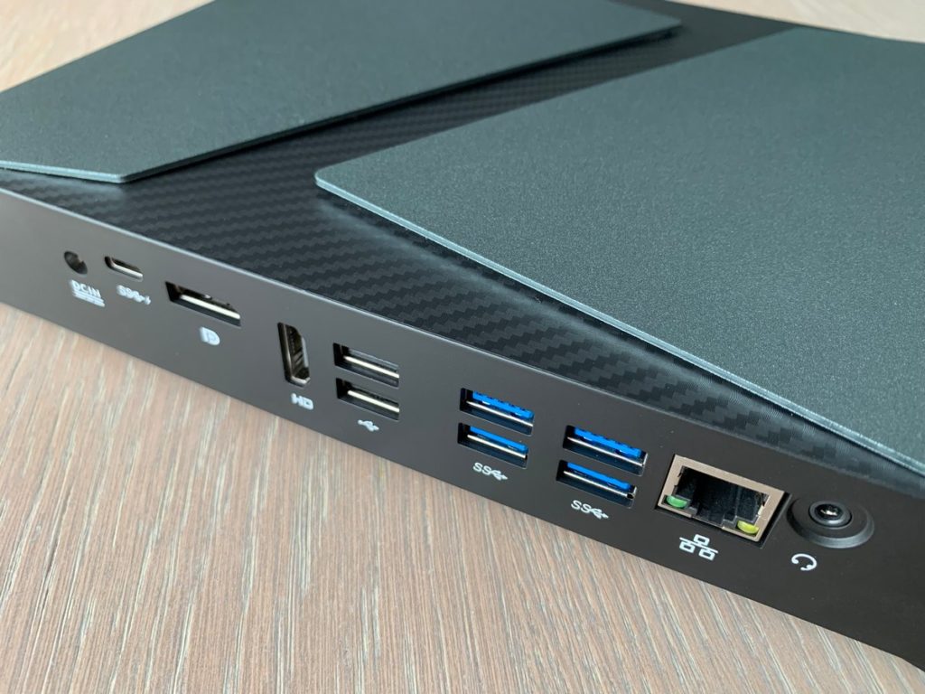 Zilliqa's Web 3.0 Gaming Console is shown in a close-up in this image. We are looking at the back of the console with numerous connection options, such as a LAN port or several USB ports. The console lies on a white wooden table and is illuminated by daylight so that no shadows are visible in the picture.