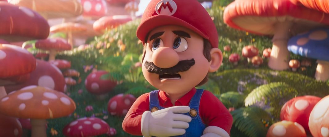 The plumber from the Mushroom Kingdom is shown in the center of the picture in the close-up with his red shirt, red cap, blue dungarees, and a brown mustache. He is standing in the middle of the day on a hilly meadow, which is covered with various large red toadstools, which we see out of focus in the background. Worried, he looks upward to the left out of the picture. At the top right of the image, a blue toadstool is also shown in the crop. This is a screenshot from the Super Mario Movie film trailer, which was released in the fall of 2022.