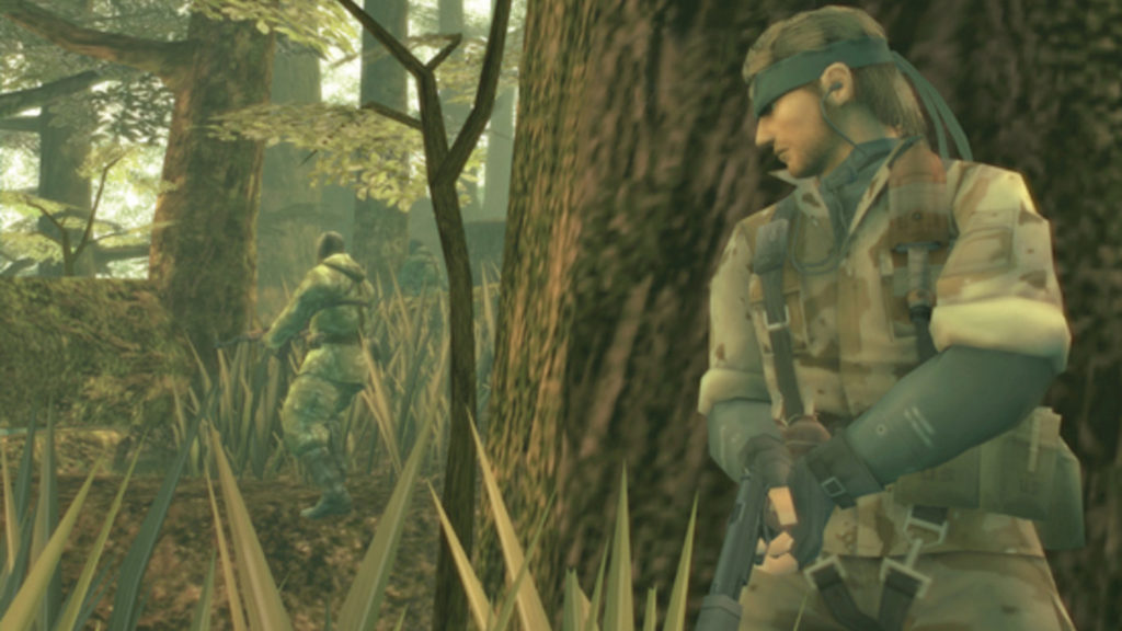 We see a screenshot from Metal Gear Solid 3: Snake Eater. This part of the series from Konami will probably get a remake. Here we see the main character in third-person view in the half-total on the right in a jungle during the day behind a large tree trunk. The protagonist wears his familiar green camouflage uniform, and a green headband and holds a pistol in both hands. His gaze is lowered and directed to the left. More mighty trees are shown in the left background and an enemy soldier in similar clothing is just patrolling to the left with a Kalashnikov in his hand. The scene is kept very greenish.
