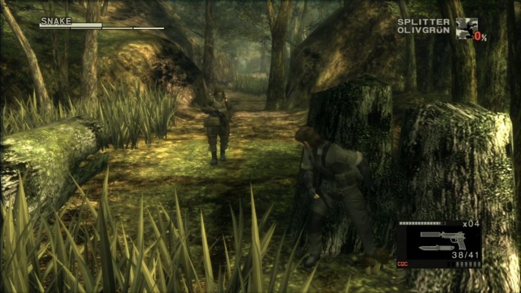 According to the latest rumors, the development studio Virtuos has been commissioned by Konami to work on a remaster of Metal Gear Solid 3: Snake Eater. Here we see a screenshot from the game back then, which sends the main character into the jungle. We catch sight of the protagonist in an olive-green uniform in the third person in total view, standing and hiding behind a tree stump on the right side of the image. His gaze falls on a patrolling soldier in a similar uniform who is walking towards us. Many trees and tall grass is shown as well as a fallen tree trunk at the left edge of the image. In the upper left corner is a horizontal bar graph with the words "Snake" in light gray capital letters. In the upper right corner is a black and white graphic with "Splinter Olive Green" next to it in light gray capital letters. In the bottom right corner, another HUD graphic is displayed, which shows the selected silencer pistol on a black rectangle, along with the ammunition indicator and the number of magazines. 