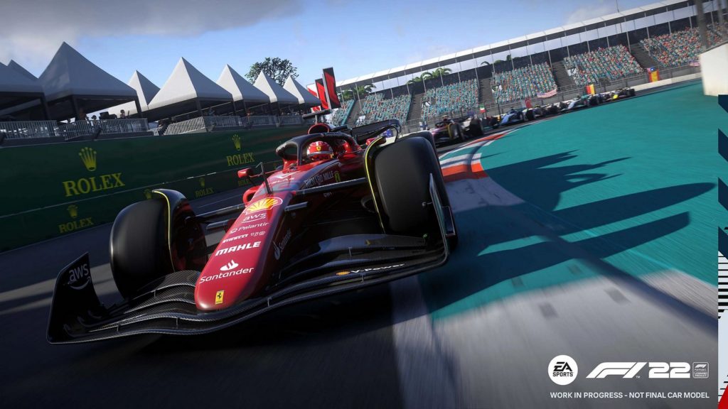 In this screenshot from F1 2022, we see a column of F1 cars in an oblique perspective from the front, which is just driving around a curve. The column runs from the top right of the background in a left turn to the front of the left half of the image and we look at an impressively designed red vehicle body, black wheels, and the driver in a wide-angle shot. On the right side of the picture, we see a turquoise infield of the stadium. The grandstand can be seen in the background with the many colorful spectators. On the left side above the race cars, we catch sight of several grayish pyramid-shaped canopies and barriers on a green-colored podium.