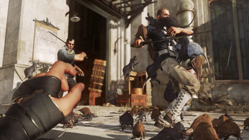 In Dishonored, you sneak through beautiful landscapes and kill people when necessary, as this screenshot shows: We're looking at the action in daylight from the player's first-person view. On a stone terrace, we have just sicced numerous black and brown rats on two saber-armed guards with the help of a learned skill. We see the many rats on the floor of the foreground image running towards the one soldier on the right side of the image, who is already trying to shake off several rats that have already taken a bite out of him. In the background, stone facades can be seen in the blur, as well as a dark entrance with wooden crates at the back left of the image.