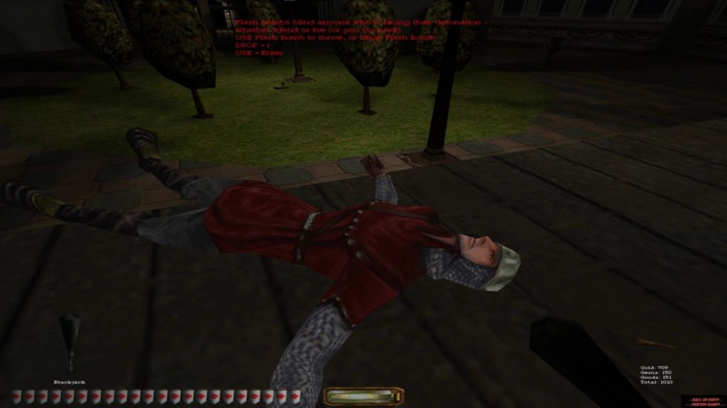We see a screenshot from the game Thief 2 The Metal Age as one of the best stealth games. At night we see a dead medieval knight in chain mail, blue robe, and helmet lying unconscious on a wooden path. We look from the player's point of view in First Person View at the unconscious knight, who has apparently just been slain with a club held in his right hand. At the bottom of the screen is the game's Interface with a prominent life meter in the form of a horizontal bar consisting of white shields with red checks. In the background, scattered trees on a green lawn can be seen in the moonlight.
