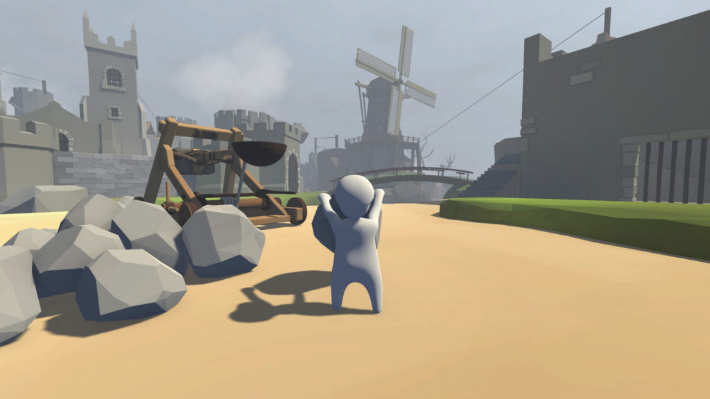 Play fun PS5 2 player games like Human: Fall Flat. Here we see a screenshot of the game, where the typical white character in third-person view is seen in the center of the image from behind, standing in daylight in front of a castle with a tall tower and a windmill. He is a white character holding a large gray stone in his hand and standing on a brown background. To his left are several stones of the same kind, and behind them is a wooden catapult, for which the stones are projectiles. The sky is slightly grayish. Enjoy this game in pairs on PlayStation 5.