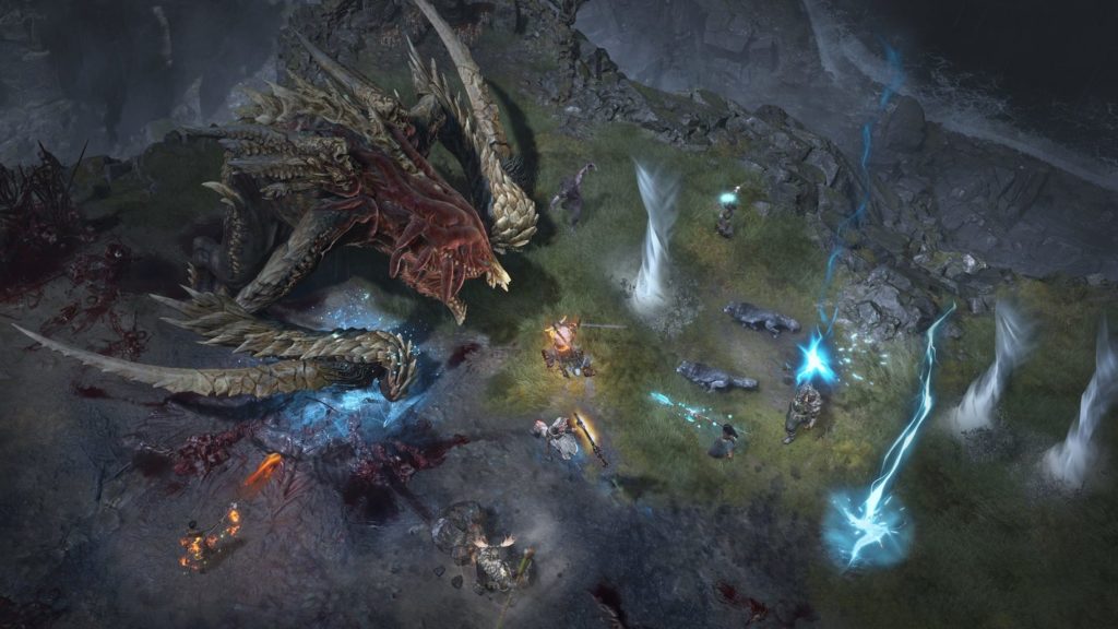 In Diablo 4 you'll not only fight against numerous hordes of undead but also against many gigantic end bosses, as seen here in this screenshot: At the top left of the image is a brownish-reddish bat-like creature with a large mouth and sharp teeth. It is standing on the edge of a partially grass-covered ledge at night. At the top of the picture, you can see the deep abyss. Around her stand 7 different players, which have a different appearance. They use blue or red colored spells or fight the creature in close combat with swords. 