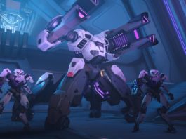 Overwatch 2 is one of the best PS5 multiplayer games. In this screenshot, we see three combat robots on standby in a spaceship-like room, which is illuminated in bluish-purple. In the center of the image, in half-profile, is a very tall white and black robot with two powerful cannon barrels. To the left and right of him are two small robots in the same posture and color. In the background, blue light shines through a hole.
