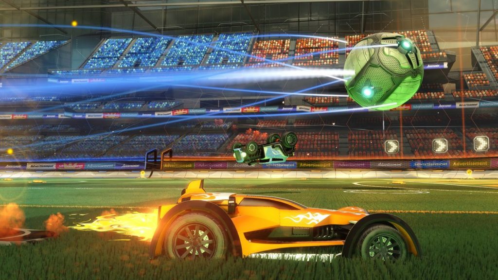 Play Rocket League in multiplayer mode and engage in intense matches with friends, as illustrated here in this screenshot, where two cars fight for the ball in a soccer stadium. In the lower half of the image, an orange sports car is shown in profile in a long shot, as it chases after a large green ball that is above it. At the same height, more in the background in the center of the picture, there is another green car that is just upside down above the ground because it is performing a somersault. In the background of the picture, you can see the grandstand, which is illuminated in blue on the left and red on the right and completely takes up the upper half of the picture running horizontally.