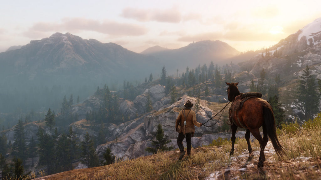 Ride your horse through the Wild West and enjoy the magnificent views of beautiful landscapes, as seen here in this screenshot: A player can be seen in a long shot view from behind in the foreground at the bottom center of the image. He leads his horse through a grassy valley illuminated by the evening sun, which consists of numerous grayish-white rocks and fir trees. In the distance, a huge mountain range can be seen, its top covered in snow. The title is one of the most beautiful open world games on PC.