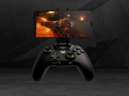 Here we see a controller from Xbox with a smartphone mounted in front of a dark background. In this way, the controller can be connected to the cell phone via Bluetooth and numerous games can be played via Microsoft's streaming service. An action FPS title can be seen on the cell phone. The background consists of a dark gray concrete-like space with angled lines and shapes. The controller has a black color and a curved ergonomic shape with the typical Xbox logo in white in the center. The two joysticks have a green base and on the right side of the controller we see the typical colorful buttons "X, Y, A, B". The game seen on the phone is a screenshot from a medieval first-person action adventure and the player is currently in a sword duel with a knight in a fiery place.