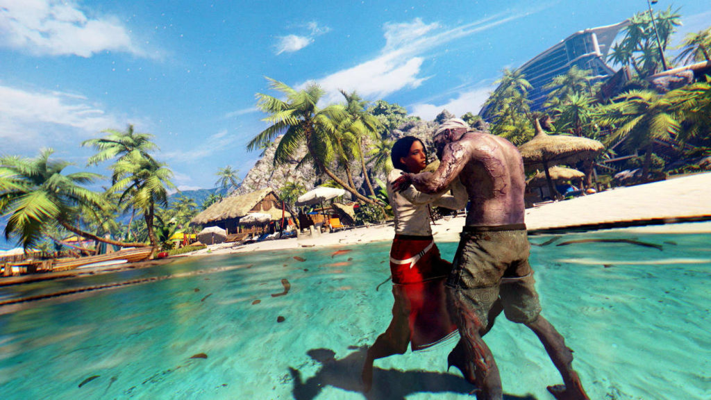 In horror co-op games like Dead Island, you experience the absolute nightmare even on dream beaches, as illustrated in this screenshot: On the right side of the image in the foreground, we see a playable female character in the daytime in a wide shot, just trying to push away a muscular zombie with short dark green pants and a bare torso, who is trying to bite the character. The two are standing in turquoise water on a sandy beach. In the background are numerous palm trees and tropical wooden huts with thatched roofs. Behind them, we recognize a rocky mountain and a glass skyscraper rising up in the upper right corner. Above it, we glimpse the bright blue sky. If you are looking for scary games to play with friends, this title is very suitable.