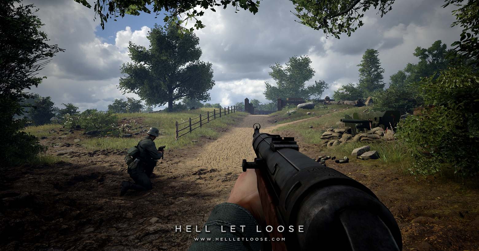 An in-game screenshot from the WWII realism shooter can be seen here. As the player, we are on the German side and are looking out in first-person view at a sandy country road, on which we ourselves are also standing. The sun is shining. To the left of the road, a little further ahead of us, kneels a German comrade who, like us, holds an MP40 in his hands and is also looking up the road. On the left and on the right green meadows, brownstones several green trees fill the picture. To our right, an anti-tank gun is pictured behind a sandbag barricade. The road in the background leads to some kind of brown masonry, which could represent an enemy base. Improve your fighting skills in Hell Let Loose with helpful tips on gameplay.