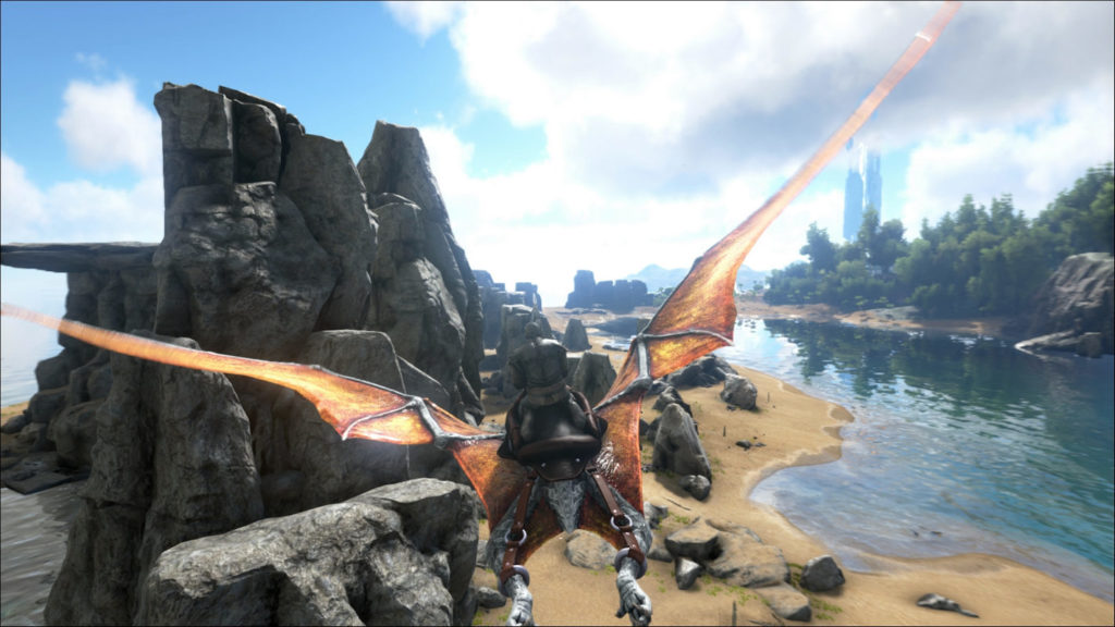An island landscape with bright sunshine, blue sky, and isolated white clouds is depicted on this screenshot. We see the player in the third-person view in the long shot in the center of the lower half of the picture. He is flying on a giant orange pterosaur over a rocky section of beach, which is surrounded by water on the left and right and runs in a fairly straight line into the background to the center of the image, where the horizon lies. On the left side of the picture, in front of the player, mighty fields rise into the sky, and on the right side, a bit further back, there is a forest running out of the picture on the right.