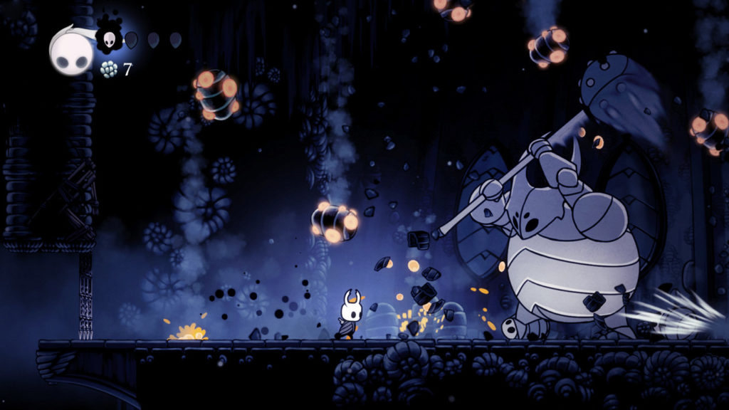 A screenshot of the 2D sidescroller Hollow Knight is shown, on which the knightly protagonist can be seen in the wide shot centered below: It’s a cute figure with small black clothes and a large white skull-like head with two horns. He is in a very dark, cold stone vault, which is decorated with numerous horn-like ornaments, which can be seen in the foreground as well as in the background. To the right of the image, we see a large white end boss with a light blue, heavily desaturated body and white protective armor around his belly, as he is about to strike with a huge stone hammer. Spherical orange glowing stones fall from the ceiling. In the background, a light blue, also strongly desaturated mist rises.