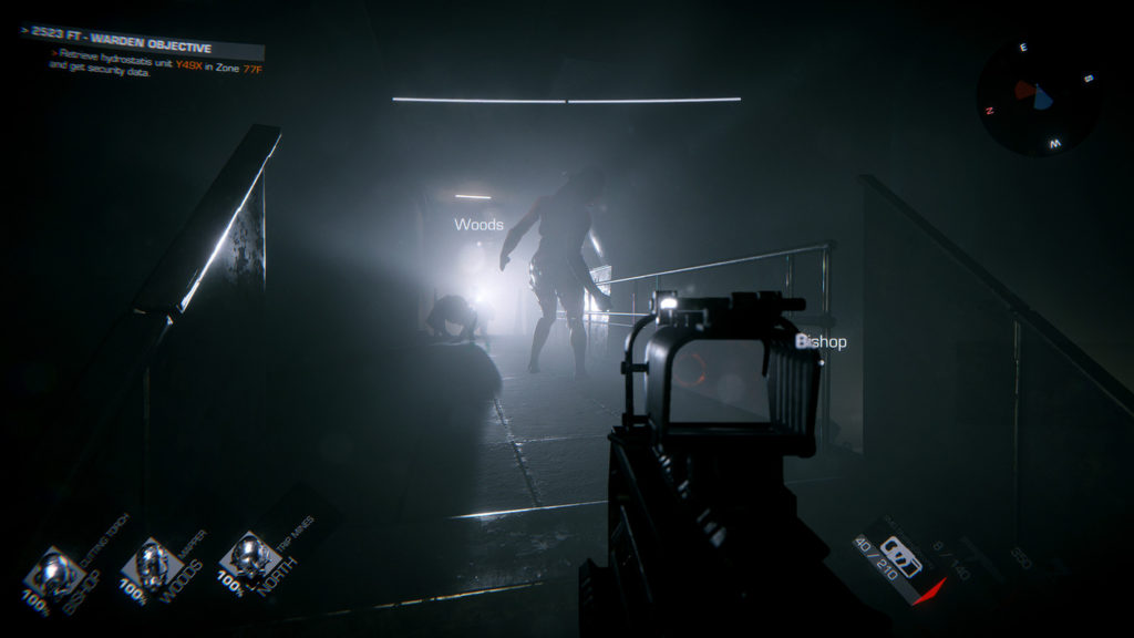 In this screenshot from GTFO, we see the player from a first-person perspective. He is in a very dark corridor that leads straight into the background to the center of the screen. At the end of the corridor, an opening can be seen through which daylight enters the room. The light reveals the silhouette of a grotesque giant creature on two legs, standing in the middle of the corridor in a long shot. Slightly leaning to the right, it slowly strides towards the player, who holds a submachine gun with a red dot sight in his hands. The avatars of three other players are displayed in the lower left corner in the back white color, and the minimap is shown in the form of a round circle in the upper right.