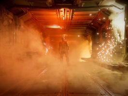 This screenshot shows a scene from the Dead Space Remake. We are on board a spaceship and are standing in the middle of a long corridor, which just runs into the background and is illuminated by an orange ceiling light. A lot of smoke is in this corridor. On the right side of the wall is an electrical device, which seems to be defective and from which a lot of sparks and smoke are coming out. At the end of the corridor, we catch a glimpse of the protagonist, Isaac Clarke, in a long shot, standing directly facing us. He has a dark combat suit and a very futuristic-looking helmet that consists of three glowing horizontal lines running parallel around the helmet. The game's release date is set and it will also be available for EA Play for free.