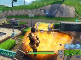 With Fortnite tips, you will learn how to behave correctly after the jump. In this screenshot, we see the player as a female character in the third person in a long shot with a brown braid, dark brown top, and orange combat pants. She is centered at the bottom of the screen and is jumping onto a roof, where she opens a golden chest with excellent loot, which is located in the center of the screen. The player is playing a map during the day and around him, there are urban structures like brown and turquoise house facades as well as a rural environment with hills on which green grass grows along with trees. The urban environment is in the image's foreground, whereas the countryside opens up in the background. Learn in a suitable guide, how to get better at Fortnite and use the best settings.