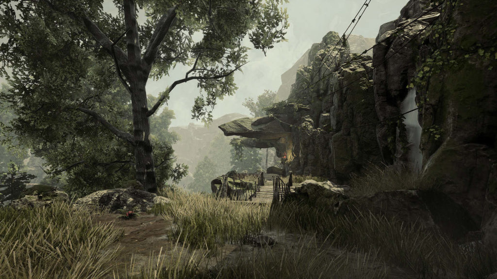In this screenshot from the upcoming Gothic 1 Remake, we see a beautiful mountain landscape in daylight with lots of grass and trees in the foreground and background. In the center of the picture, we see a wooden suspension bridge, which leads to a small camp under a rock. There a torch is burning. To the right of the camp, we can see a waterfall.