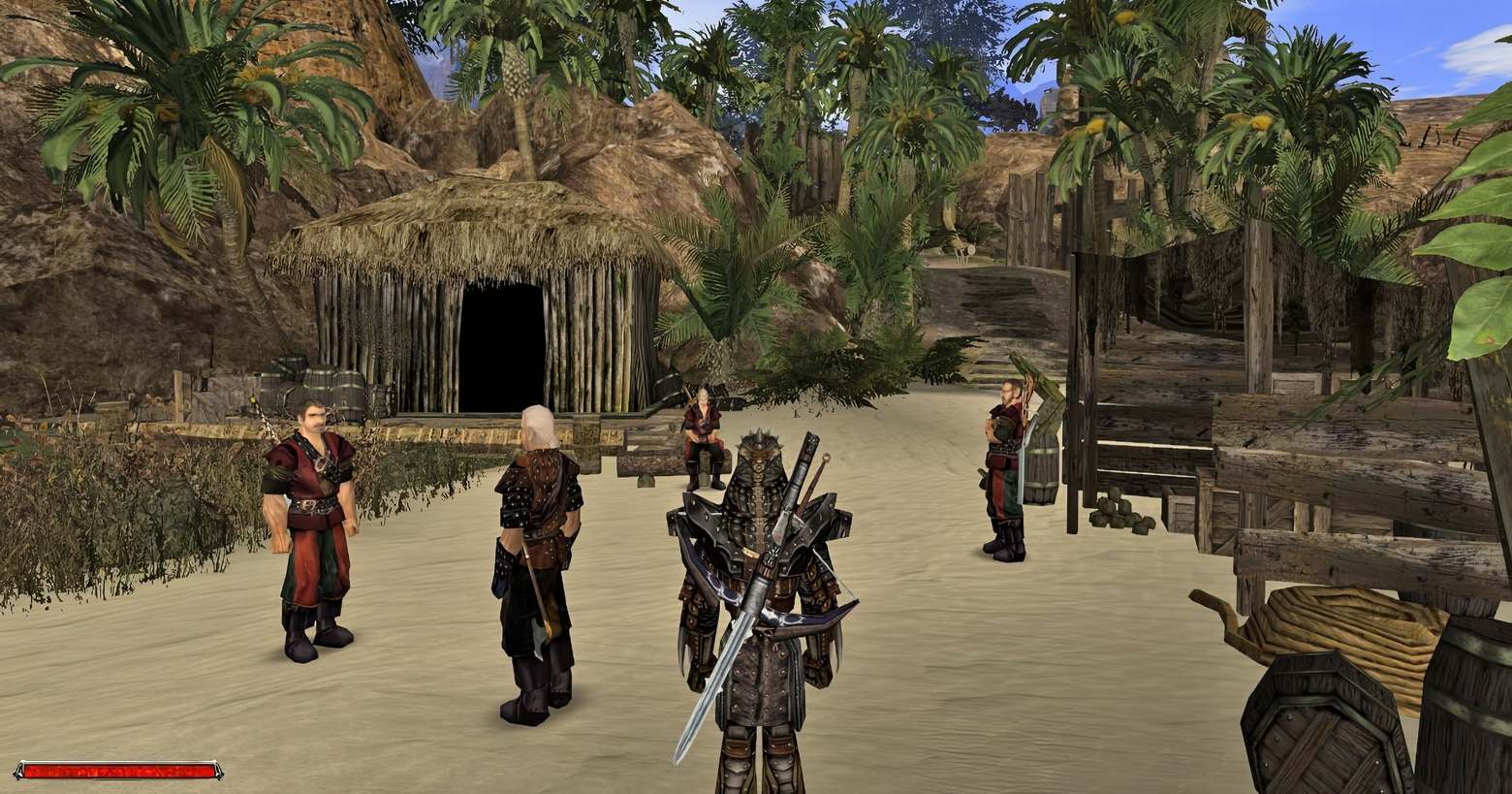 This screenshot shows the player in a third-person mode in the wide shot at the bottom center of the screen. He wears a brown leather-like armor with very rigid shoulder pieces. On his back, he carries a very long iron sword. He stands in the daytime in a medieval village in a palm landscape with sandy soil. At the back left a wooden hut with a thatched roof is depicted. Directly in front of him are four characters standing around looking at each other. On the right, wooden objects such as barrels can be seen and brown rocks rise in the background. At the bottom left, we again see a plain red health bar, but this time much smaller in the corner. At the top of the image, we can see the blue sky with scattered clouds. Gothic 1+2 for Nintendo Switch will probably be released in 2023.