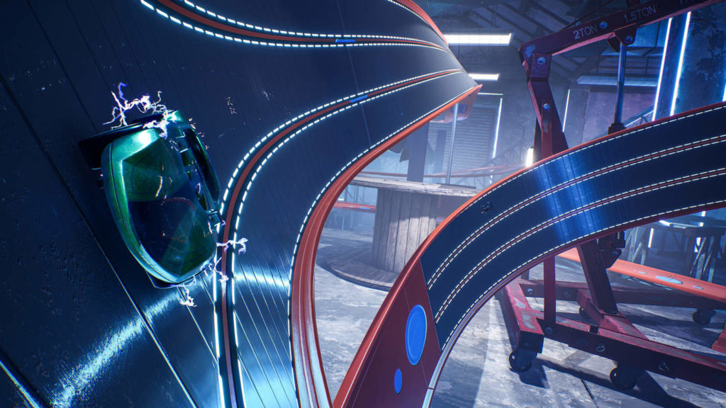 In this screenshot from Hot Wheels Unleashed, we see a blue race track with red marker lines. The track is tilted extremely to the right and comes from the background running from the top of the image to the front at the bottom left. A similar track section can be seen on the right side of the image, where the track curves from the bottom to the top right. All in all, the picture is very much filled with this racetrack. On the left side we can see a green racing car in toy optics, as it drives straight along the race track tilted to the right. In the background, we glimpse the facade of a warehouse, which makes it clear that these are toy cars.