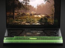 This screenshot shows an RTX 40 series laptop running one of NVIDIA's latest Geforce GPUs. The laptop is shown in the center of the picture and a game clip can be seen where the player is in a breathtaking forest landscape. The background is kept simple in a grayish tone. This is a 3D visualization where the keyboard has been deliberately omitted so that we can look inside the laptop. The bottom edge of the laptop is highlighted with a typical Nvidia green grid.