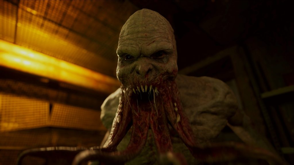 Stalker 2 also includes many bloodthirsty creatures and mutants, as the gameplay trailers of the game show. In this screenshot, we as the player are looking right into the ghastly pale face of a vicious creature, which can be seen in a close-up in the center of the image. It looks at us with an evil face and a wide-open mouth. We can see the many pointed teeth and bloody tentacles hanging from its mouth, which look extremely grotesque. We are in a dark corridor, which is only illuminated by an orange neon light from the left.