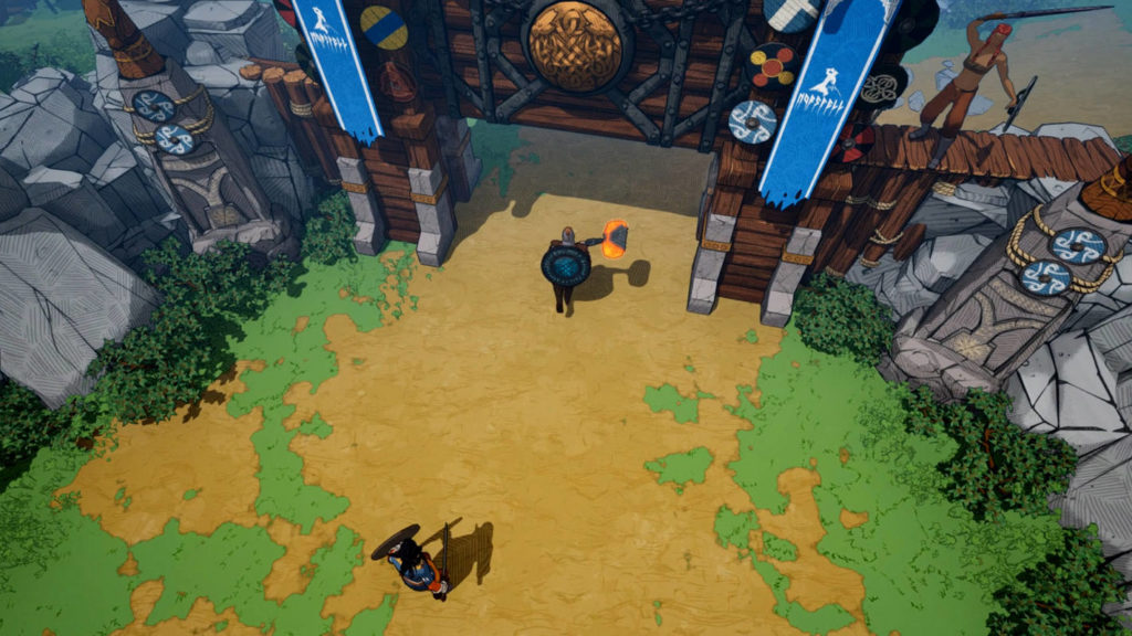 From an isometric perspective, we see two playable Viking characters during the day on a yellow path coming from below and going up to an open wooden gate that belongs to a Viking camp. One player can be seen at the bottom of the screen in the center. He is wearing blue armor and has black hair, and red pants. He is armed with a sword and a round shield. The second Viking is standing just in front of the gate in the center of the picture. His large blue round shield is mounted on his back and covers his entire upper body. In his hands, he holds a huge fiery glowing hammer. Two blue banners are attached to the gate on the left and right, and palisade walls extend from the gate to the sides. To the left and right are gray rocks and off the path, we see grass and bushes.
