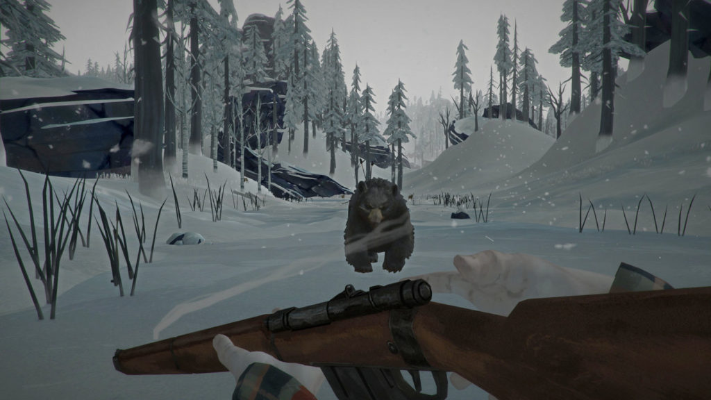 In this screenshot from the Long Dark, we as the player are standing in a snowy valley armed with a carbine in the first-person perspective. We are reloading our weapons, while a wild bear runs towards us, which we can see in the center of the image. Our hands can be seen at the bottom of the picture, pale from the cold. To the left and right of the picture are numerous very tall fir trees, which are also shown in great numbers in the background. It is snowing and the sky is heavily overcast, creating an oppressive sunless mood.