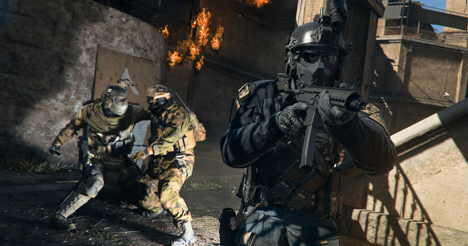 An armed soldier in a black uniform from Warzone Season 2 walks in our direction, while in the background two soldiers are in close combat.