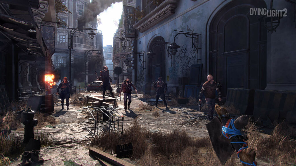 We see five players walking towards the camera with melee weapons in a desolate alley in the city during the day.
